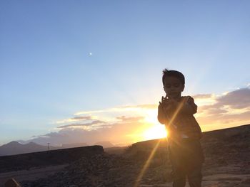 Boy standing against sky during sunset