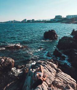 Young woman lying on rocks at beach against sky