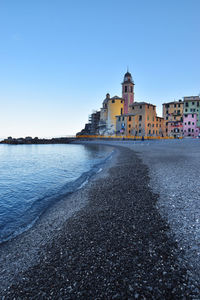 Buildings by sea against clear blue sky
