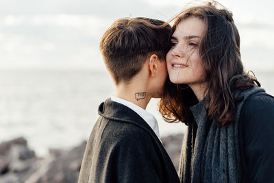 Lesbian women embracing while standing against sea