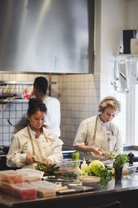 Female chefs preparing food against male colleague in kitchen at restaurant