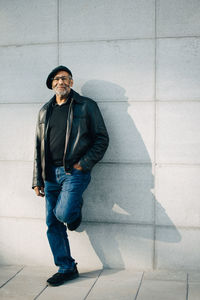 Full length portrait of senior man standing against wall