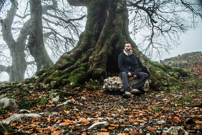 Full length of man sitting on rock at forest