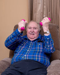 Smiling man exercises with small barbells from the comfort of his living room chair