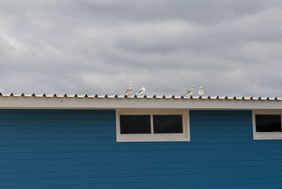 Birds perching on building against cloudy sky