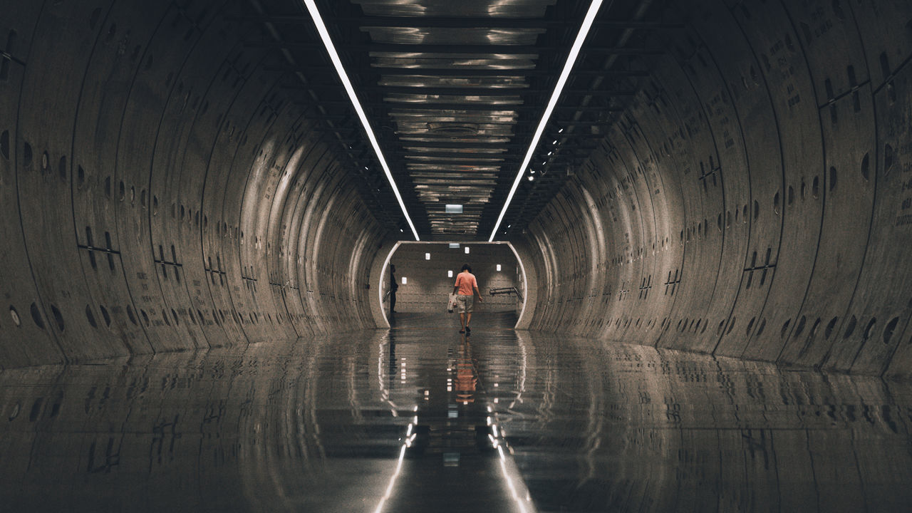 REAR VIEW OF WOMAN WALKING IN TUNNEL