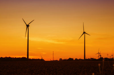 Silhouette wind turbines on the field against the sky during sunset