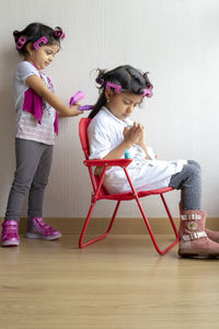 Girl styling hair of sister sitting on chair at home