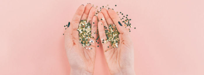 Close-up of hands holding decoration against pink background