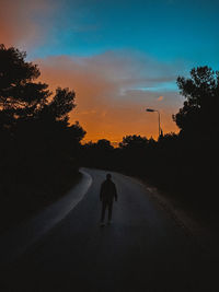 Silhouette man on street against sky during sunset