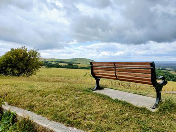 Empty bench on field against sky