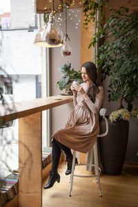 Woman holding coffee cup sitting on chair in cafe