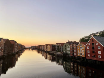 Buildings by river against sky during sunset