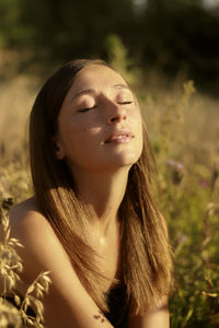 Close-up of beautiful woman with eyes closed sitting on field during sunset