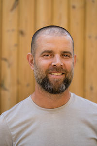 Portrait of the handsome man with beard smiling standing against wooden background