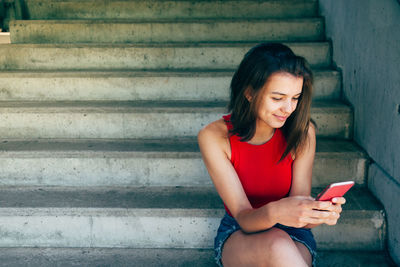 Young woman using mobile phone while sitting on staircase