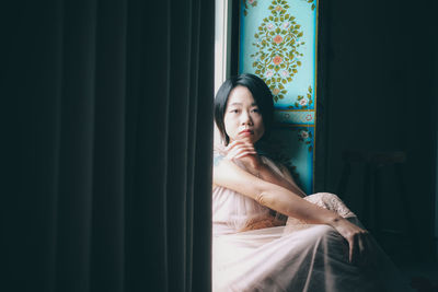 Portrait of young woman standing against curtain