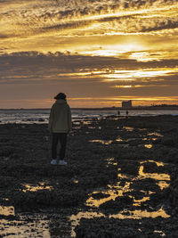 Rear view of woman walking at beach against sky during sunset