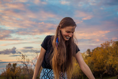 Young woman smiling while standing against sky during sunset