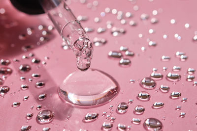 Pipette, drop and splashes of micellar water on a pink background.