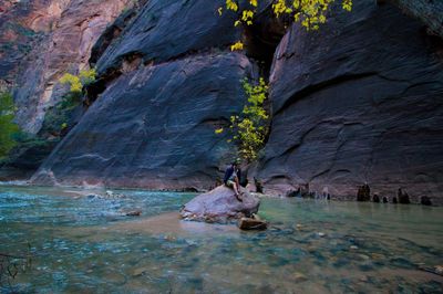 Man sitting on rock at lake against mountains