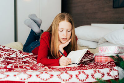 Girl writing in diary while lying on bed at home