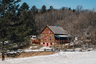 Houses on snow covered field by trees against mountain