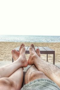 Low section of people relaxing on beach against clear sky