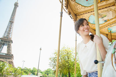 Portrait of smiling young woman standing at amusement park against sky