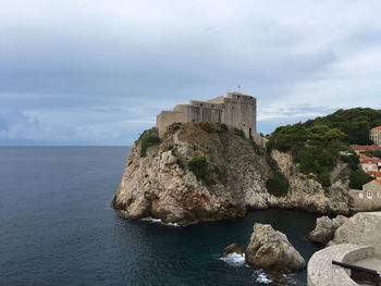 Castle on cliff by sea against sky