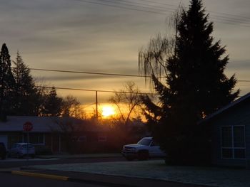 Cars on road by buildings against sky during sunset