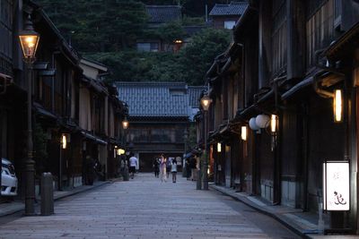 People walking on street amidst houses at dusk