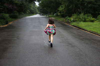 Rear view of woman walking on road amidst trees