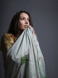 Thoughtful beautiful woman holding shawl against gray background