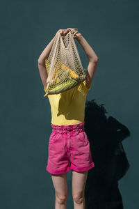 Woman holding mesh bag in front of face standing near wall