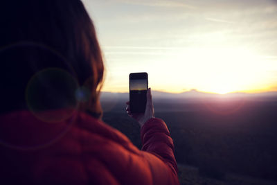 Rear view of woman photographing landscape with smart phone during sunset