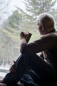Side view of mature man with coffee sitting on window sill