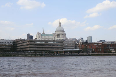 Buildings by river against cloudy sky