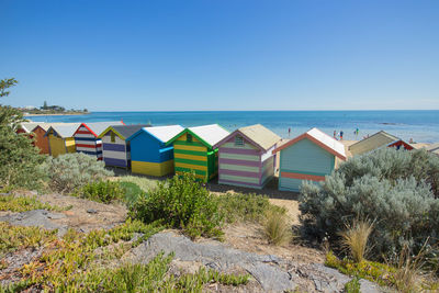Beach huts by sea against clear blue sky