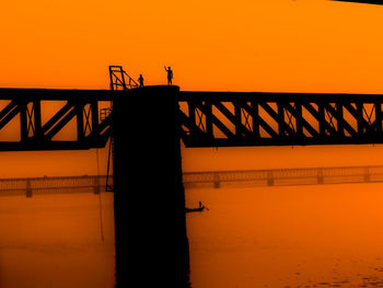 Silhouette bridge over sea against orange sky