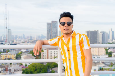 Young man wearing sunglasses standing against cityscape