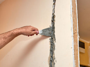 Close-up of hand holding wood against wall