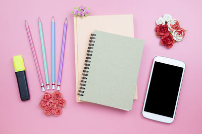 Directly above shot of books and mobile phone on pink background