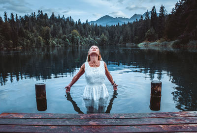 Woman standing by lake against trees