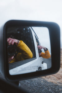 Reflection of people photographing on side-view mirror