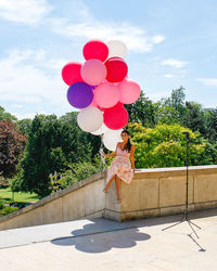 Rear view of woman with balloons standing against trees