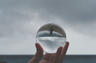 Close-up of hand holding crystal ball against sky