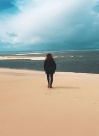 Rear view of young man standing on beach against cloudy sky