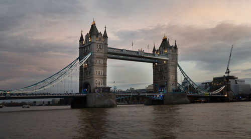 Suspension bridge over river against cloudy sky