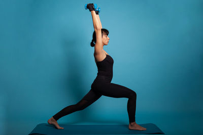 Full length of woman exercising against blue background